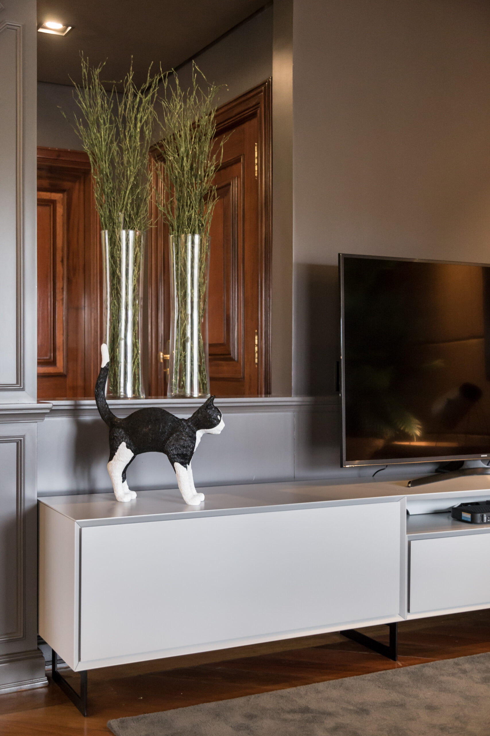 detalhe da sala com gato de porcelana, aparador branco e televisão